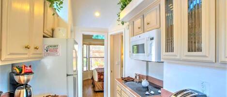 A narrow kitchen with white cabinets, a coffee maker, a microwave, and a toaster.