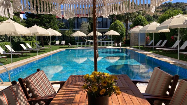 Un espace aménagé au bord de la piscine, avec une table en bois, des chaises à rayures et un pot de fleurs orné de fleurs jaunes.
