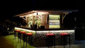 Un espace bar extérieur doté d’un comptoir en pierre, de tabourets de bar rouges et d’un mur recouvert de carreaux.