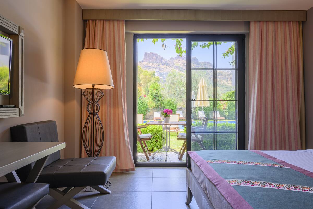 A hotel room with a bed, a desk, a chair, a table, and a view of the outdoors.