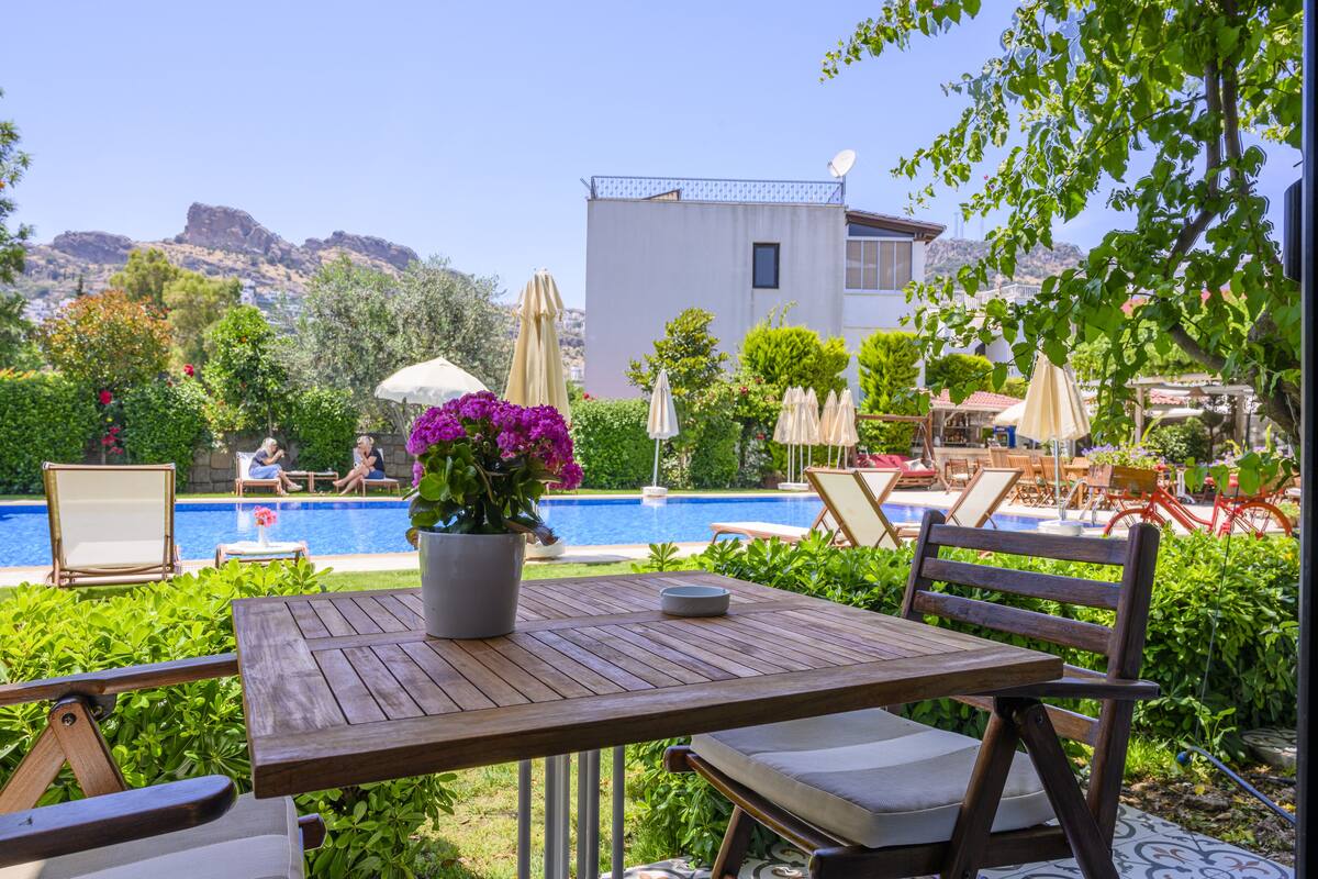 A poolside area with a wooden table, chairs, and a potted plant with purple flowers.