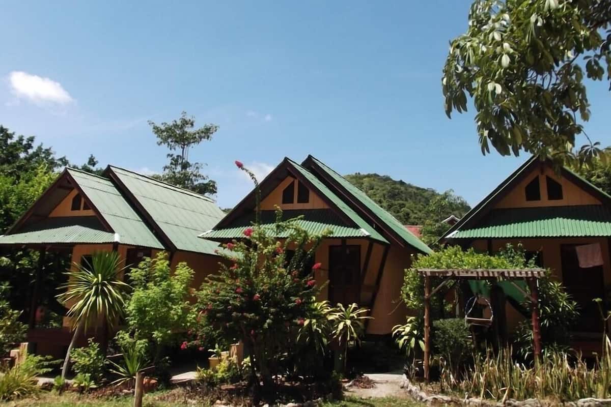 A row of cabins with green roofs, surrounded by lush greenery and a clear sky.