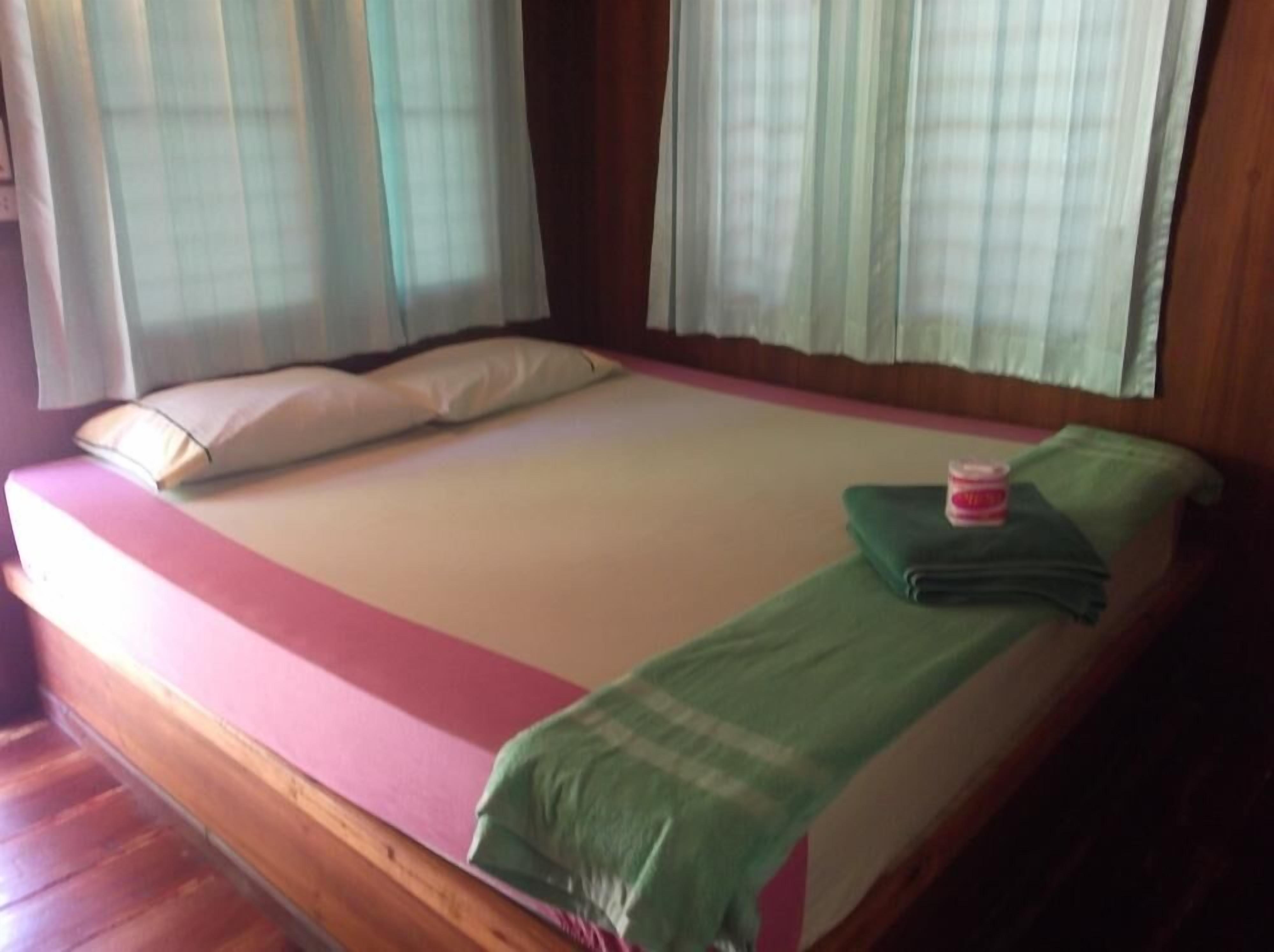 Una cama individual con una colcha rosa y blanca, una manta verde y una almohada.