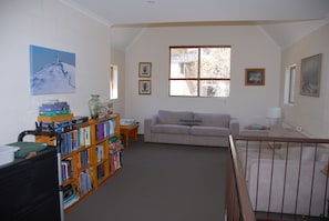 A living room with a bookshelf, a sofa, and a window. - Summit Ridge Alpine Lodge (Falls Creek)