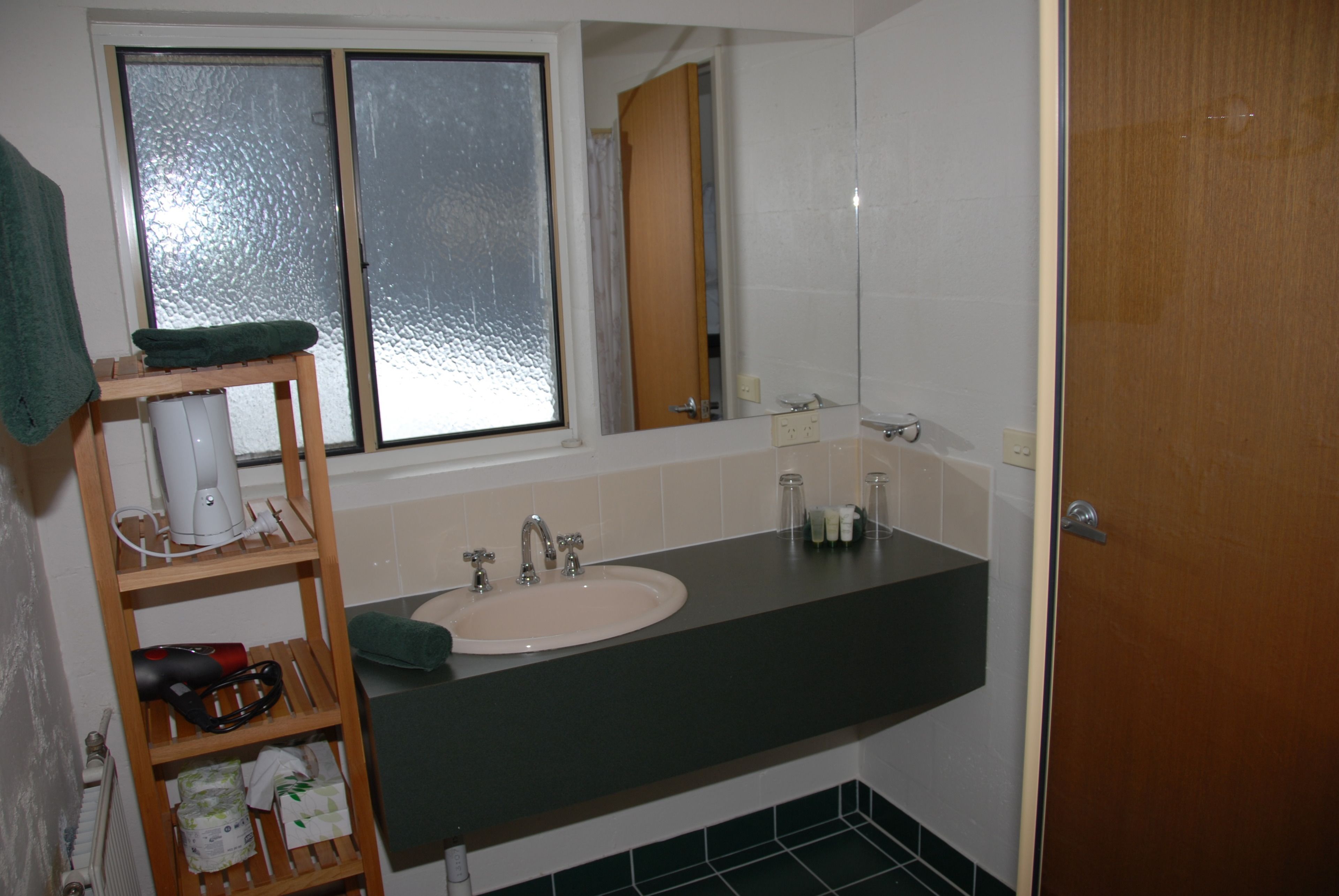 Une salle de bain équipée d’un lavabo, d’un miroir et d’une étagère où sont rangés les articles de toilette.