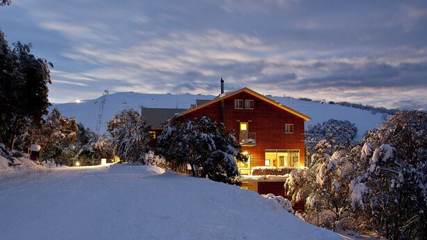 A two-story wooden house with a balcony, surrounded by snow-covered trees and a mountain in the background. - Summit Ridge Alpine Lodge (Falls Creek)