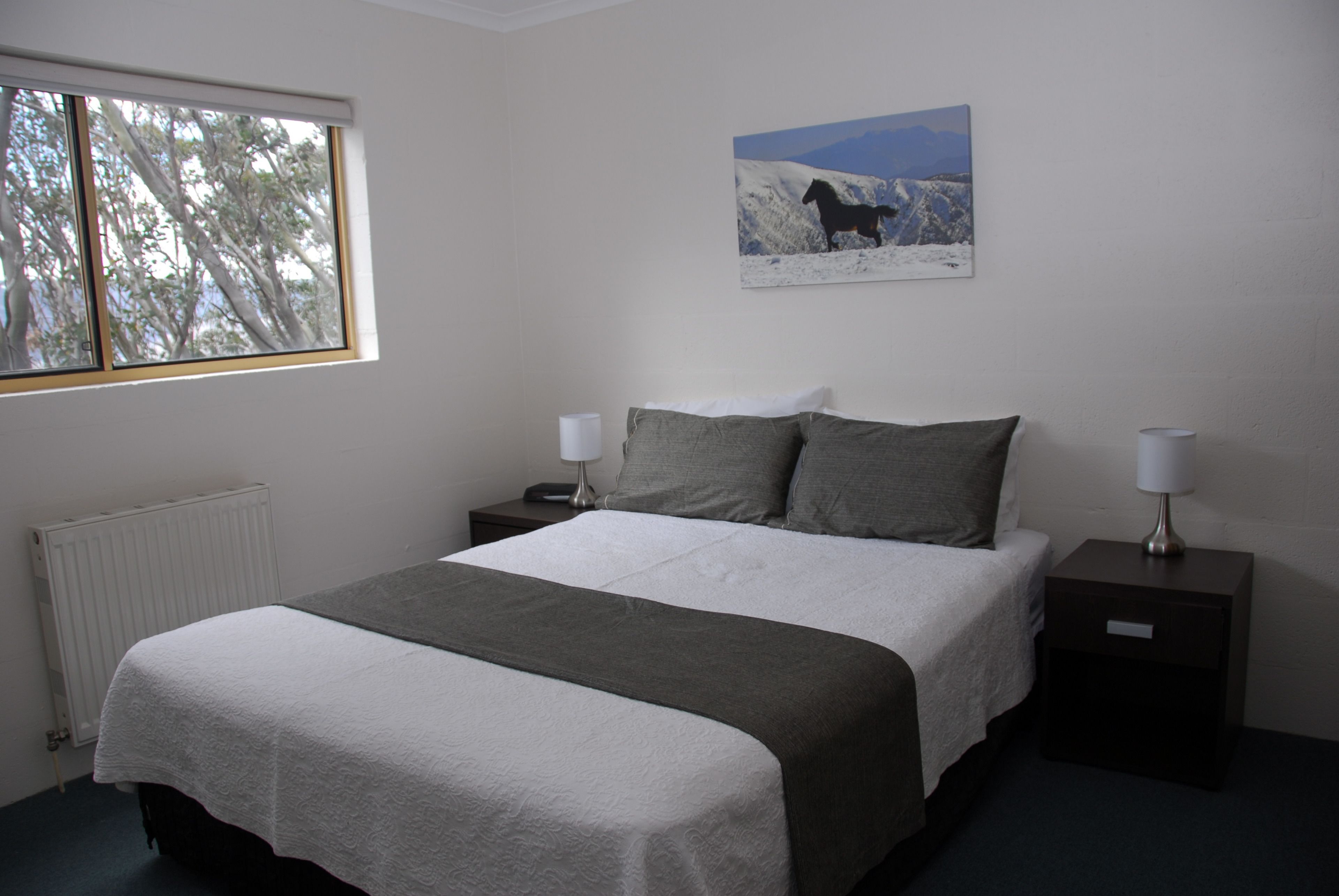 A bedroom with a bed, two bedside tables, a window, and a wall-mounted painting.