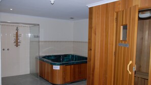 A bathroom with a glass-enclosed shower, a wooden bathtub, and a wooden door with a sign. - Summit Ridge Alpine Lodge (Falls Creek)