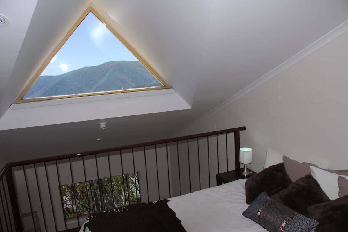 A bedroom with a skylight, a bed, a nightstand, and a view of mountains.