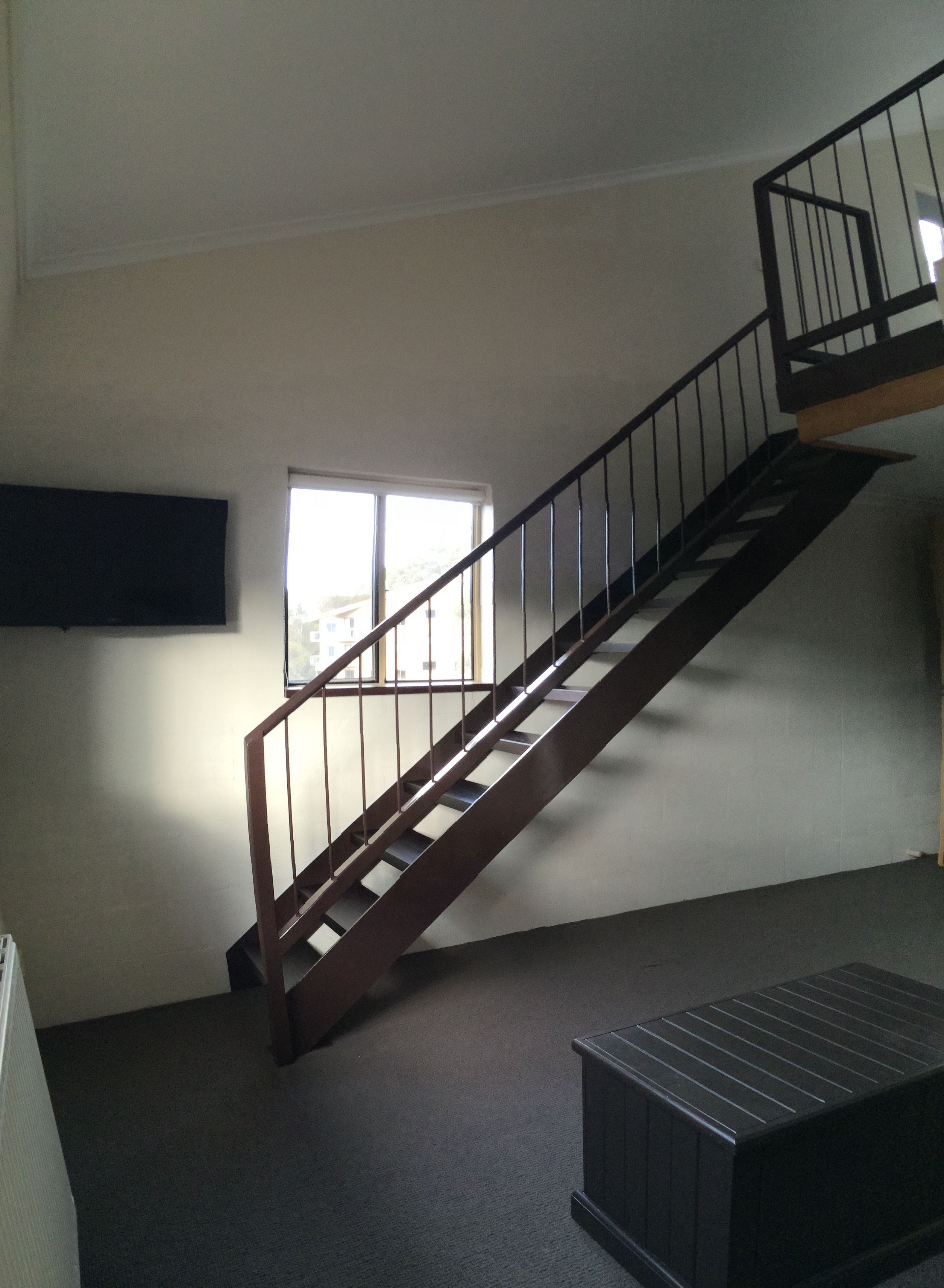 A staircase with a wooden handrail and metal balusters, leading to an upper floor. A window provides natural light to the room.