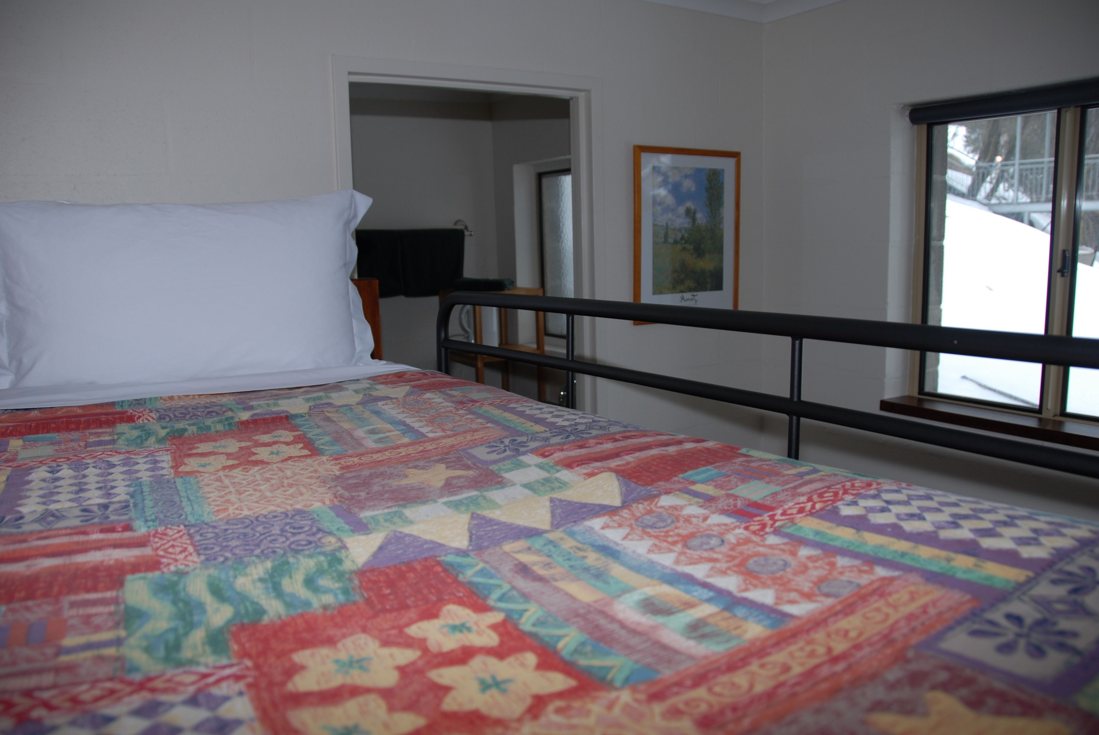 Un dormitorio con cama, un colcha colorida, una ventana y una puerta que da a otra habitación.