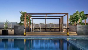 Un área de piscina exterior moderna con una estructura de pérgola metálica, sillones de descanso y piscina con baldosas.