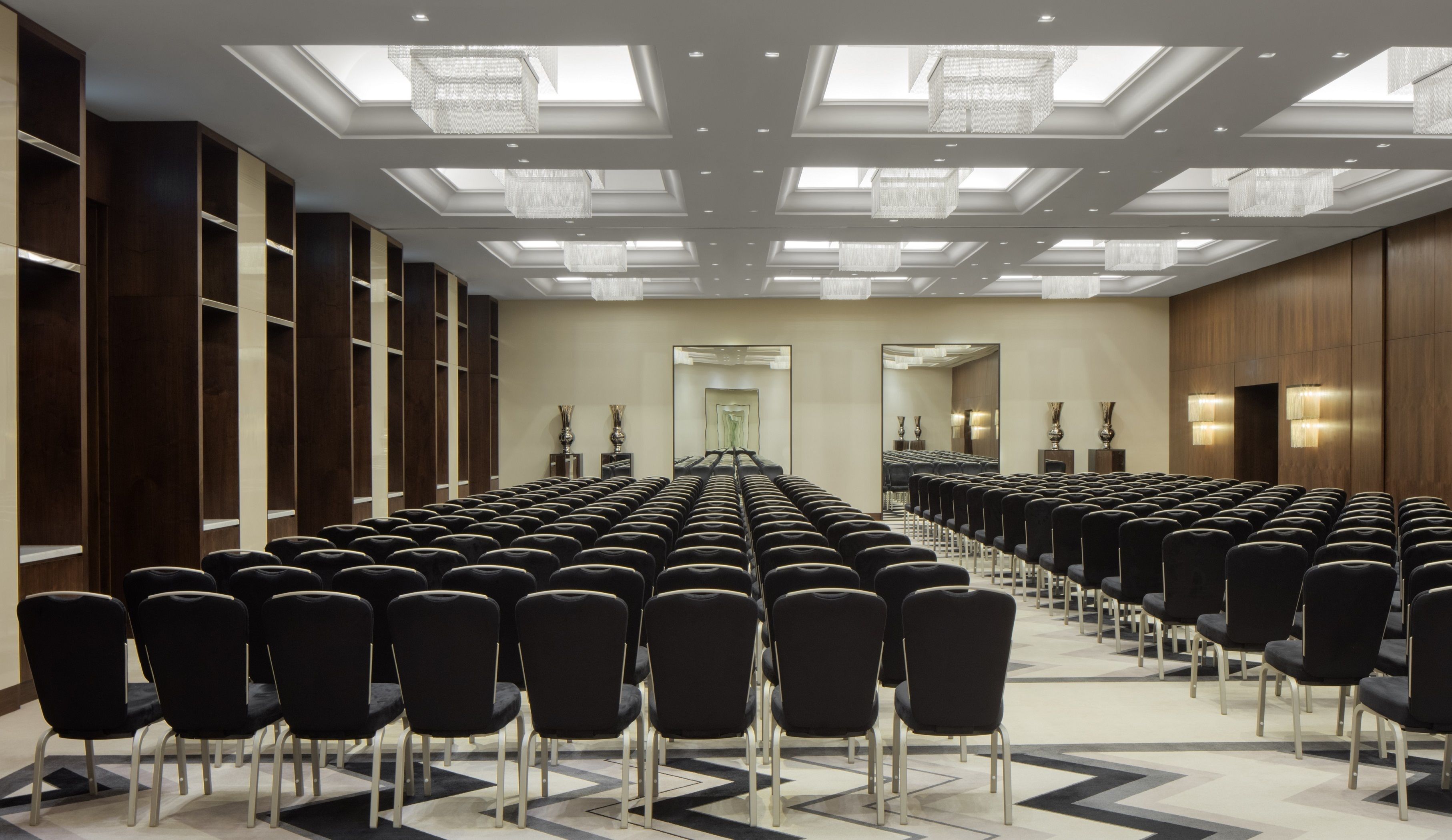 Une salle de conférence avec des rangées de chaises noires, un plafond haut doté de lucarnes et des panneaux de bois recouvrant les murs.