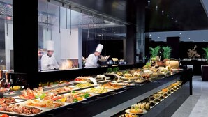 Un bufé con diversos platos, un chef al fondo y una decoración moderna.