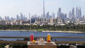 Una mesa de comedor con sillas en un balcón que da a un horizonte urbano y una masa de agua.