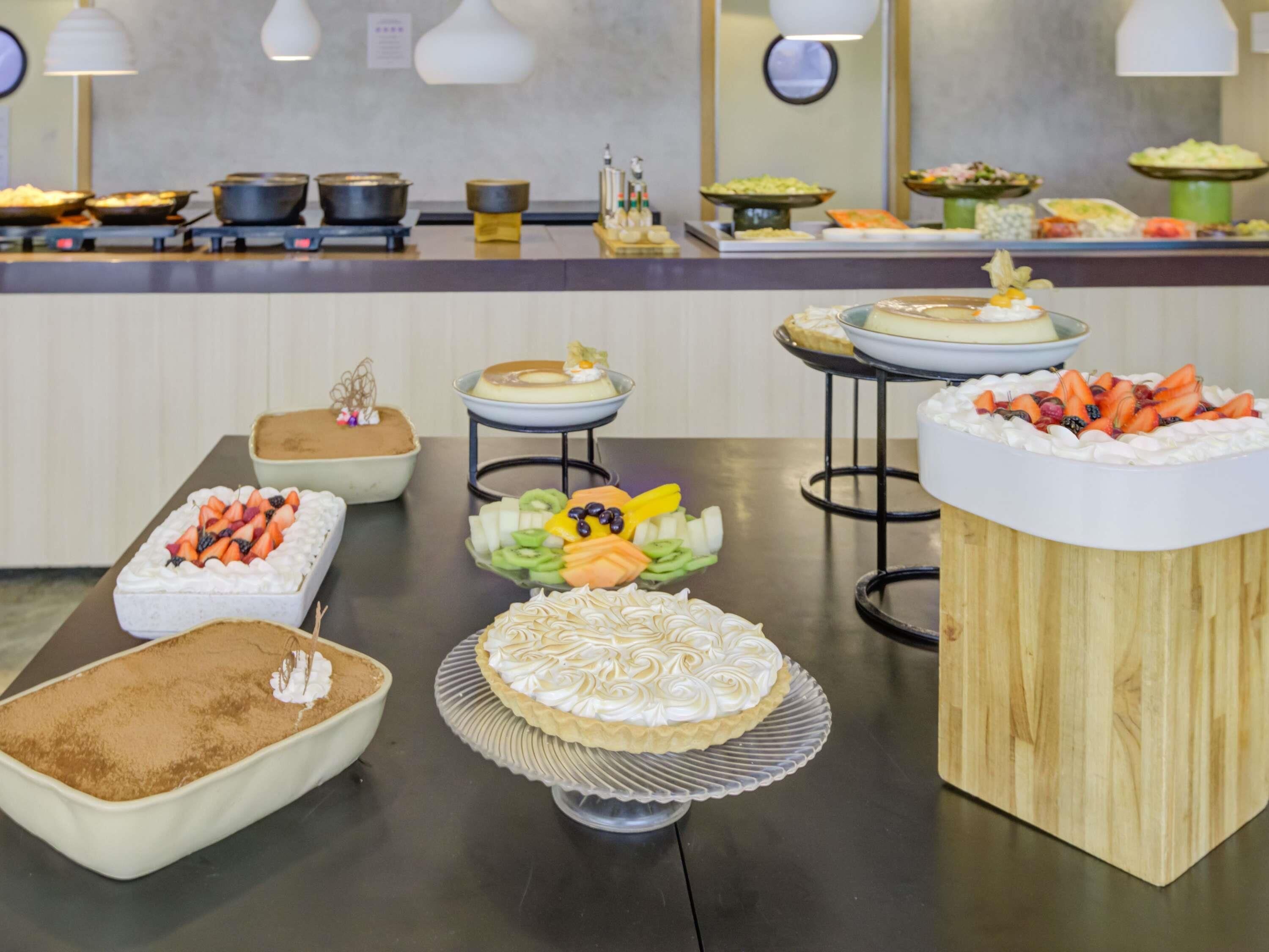 A buffet with various desserts and dishes, including a pie with whipped cream and fruit, a cake with a decorative top, and a variety of other desserts.