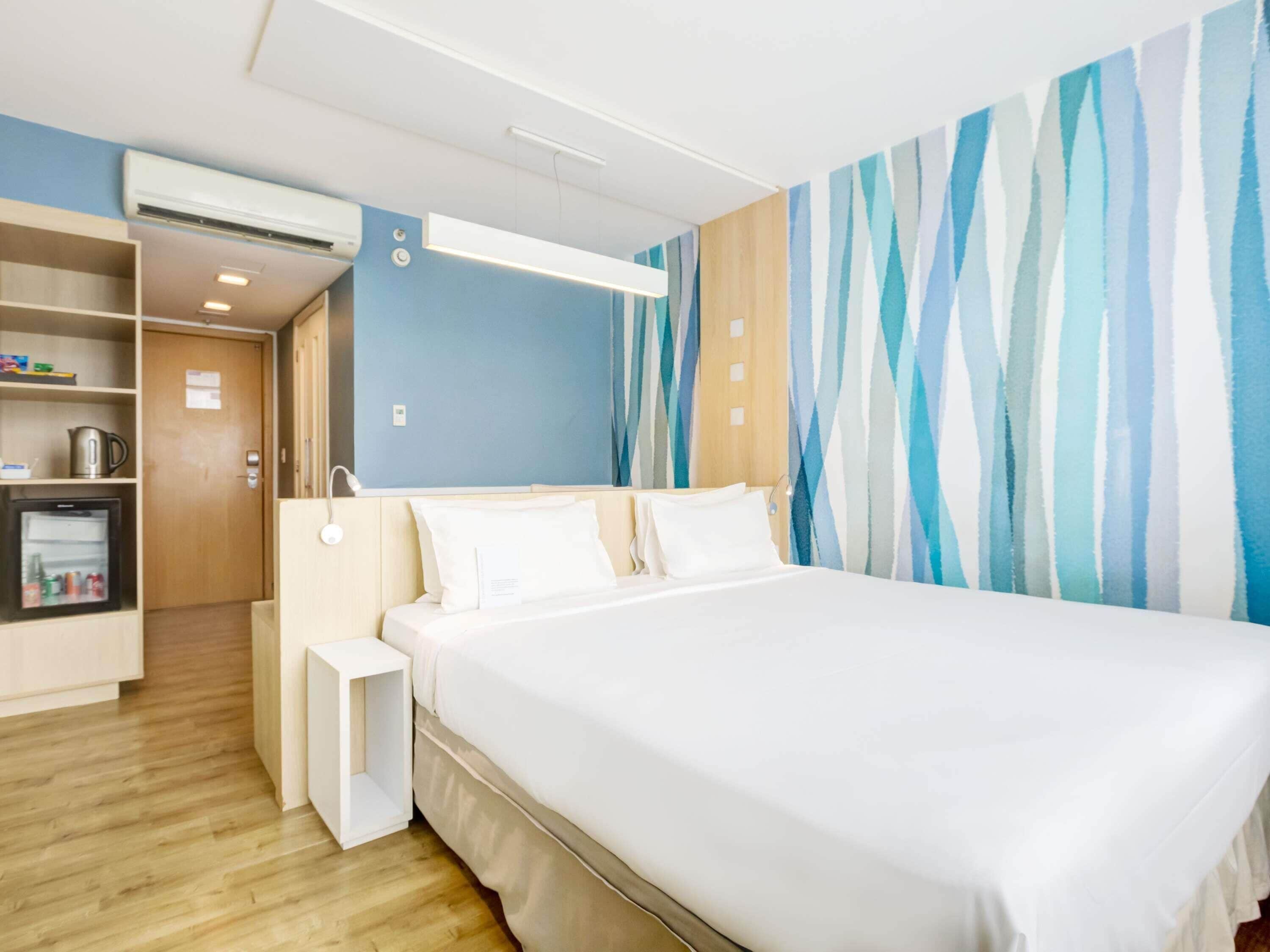 Habitación de hotel con cama, mesita de noche, armario y pared con diseño a rayas.