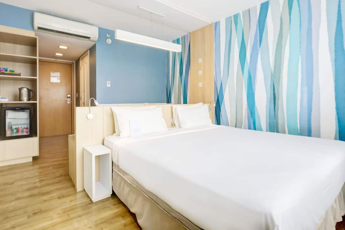 Hotellihuone, jossa on sänky, yöpöytä, vaatekaappi ja raidallinen tapetti.