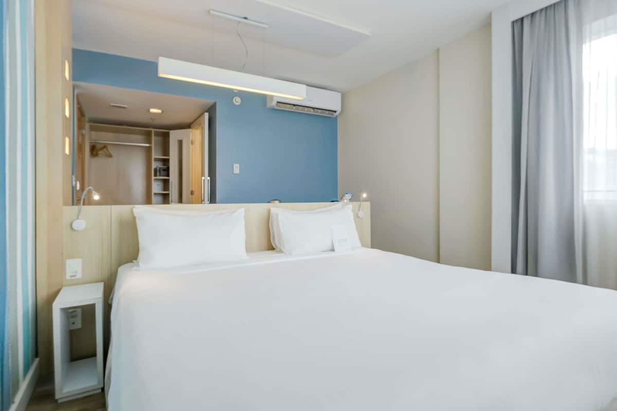 Hotellihuone, jossa on suuri sänky, yöpöytä, vaatekaappi ja peili.