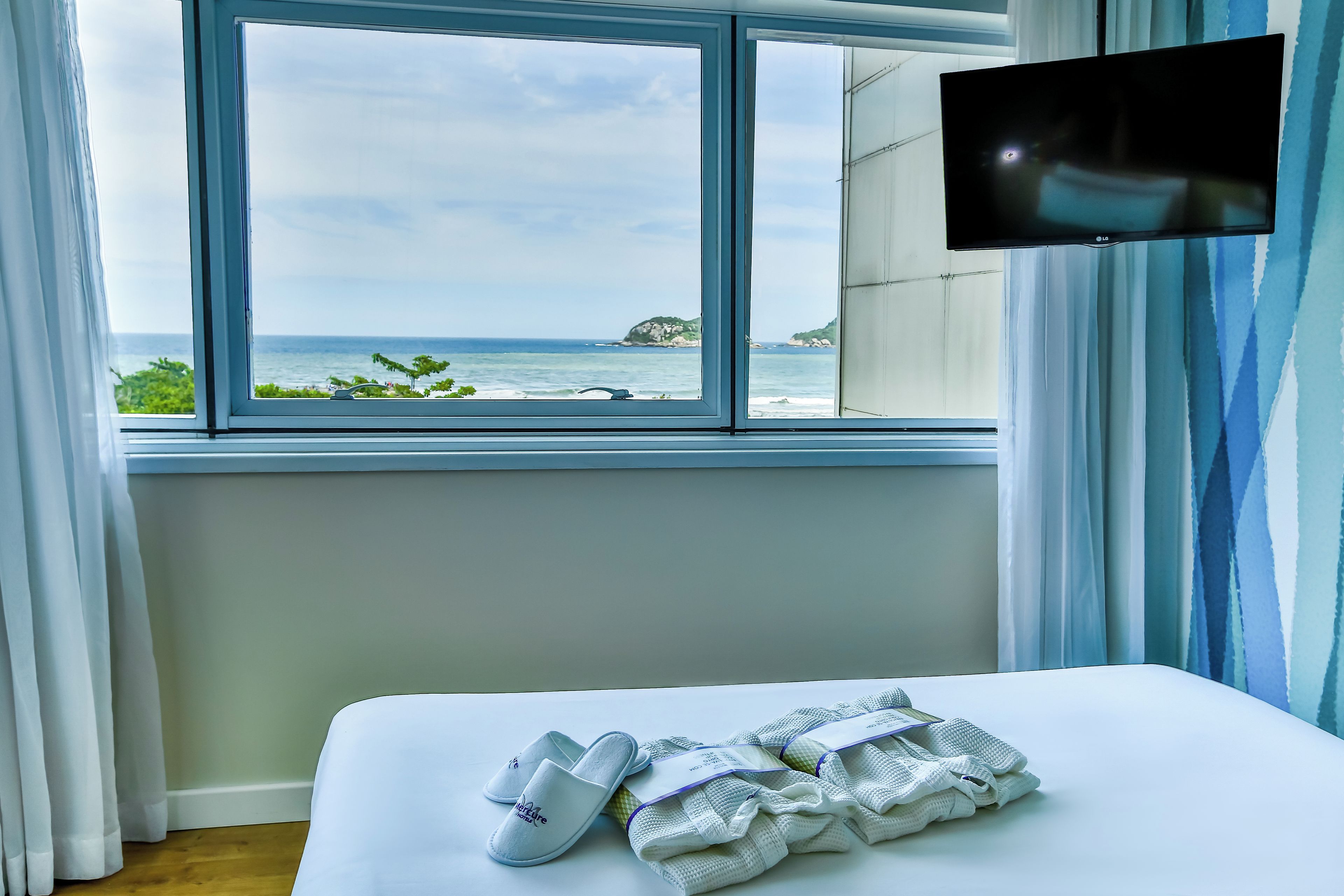 Una habitación de hotel con una cama, un televisor en la pared y una ventana con vista al mar.