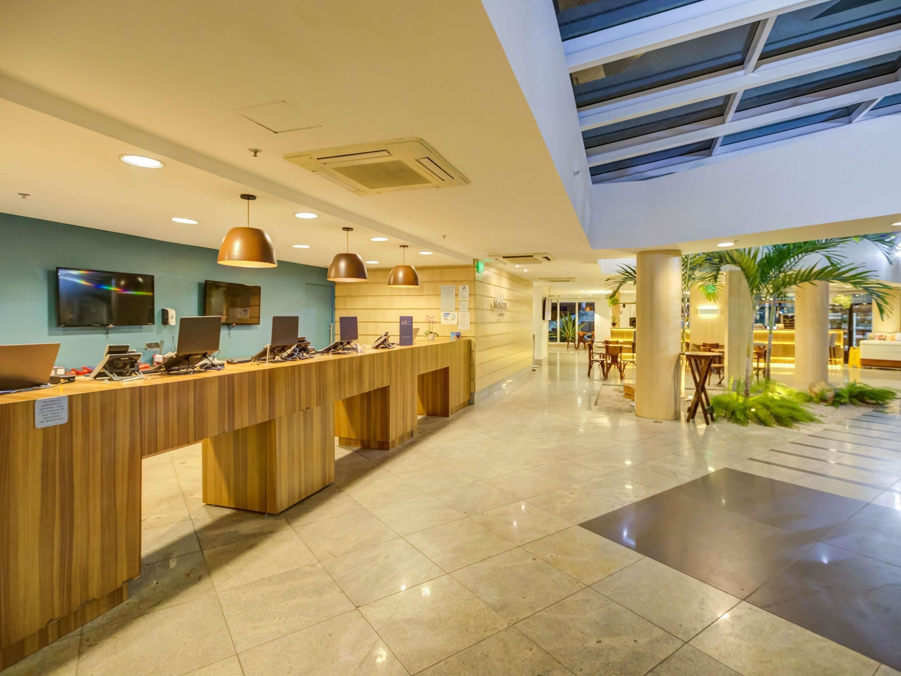 A modern hotel reception area with a wooden reception desk, multiple computer stations, and pendant lighting.
