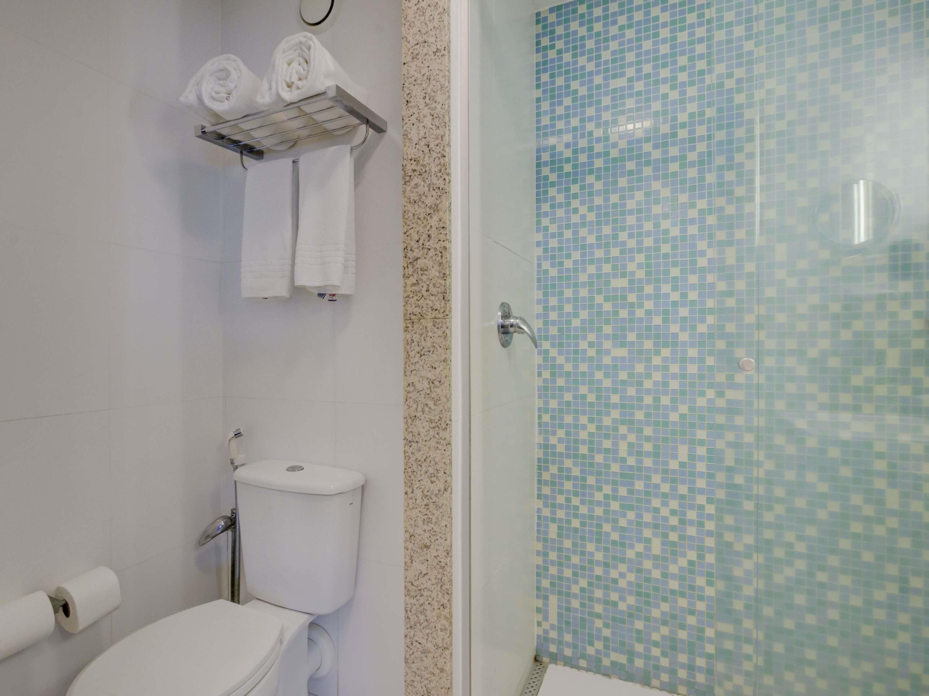 A bathroom with a toilet, a sink, a glass shower enclosure, and a towel rack with towels.