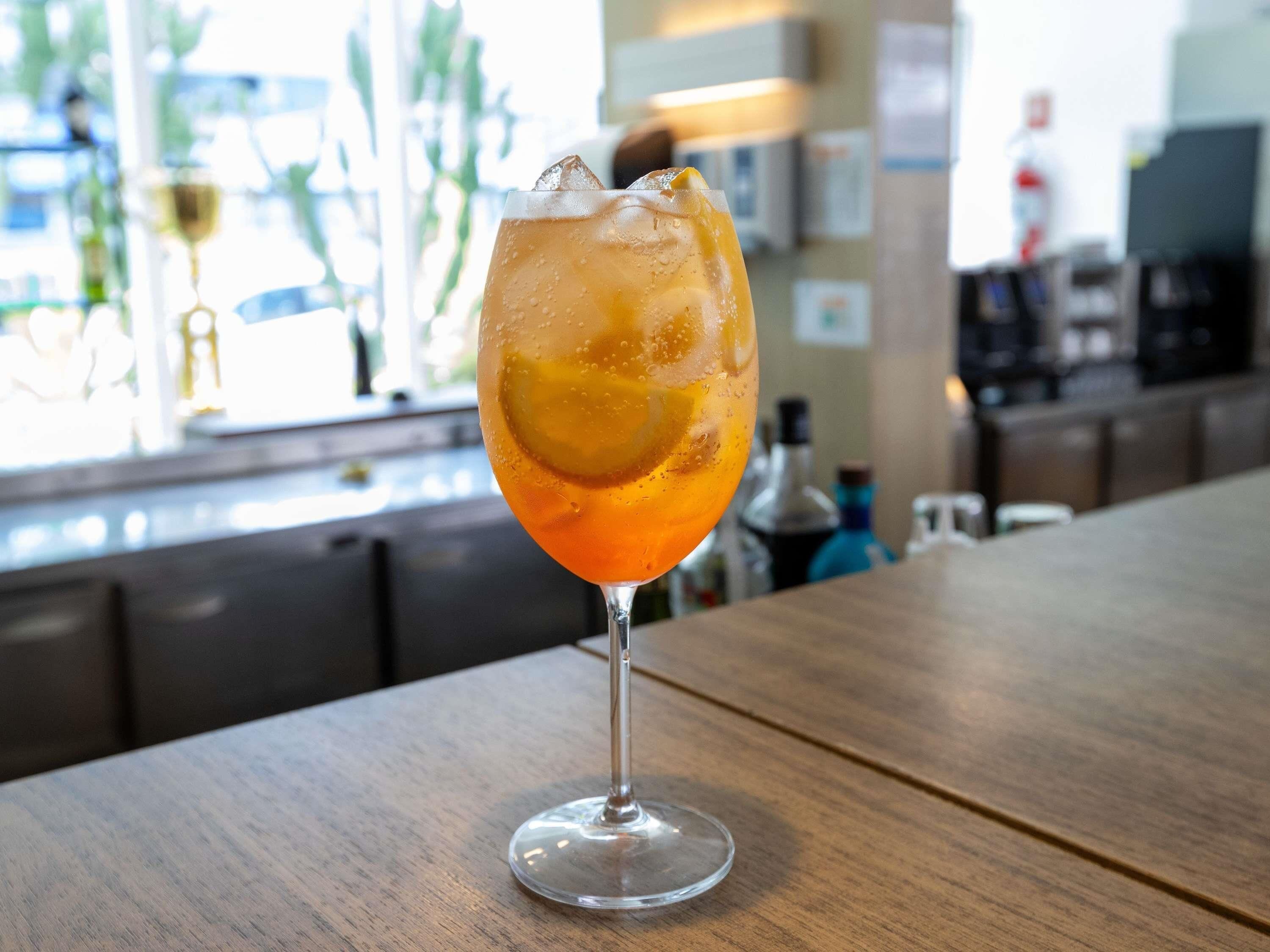 Un verre d’une boisson ambrée, avec des glaçons, posé sur le comptoir en bois d’un bar.
