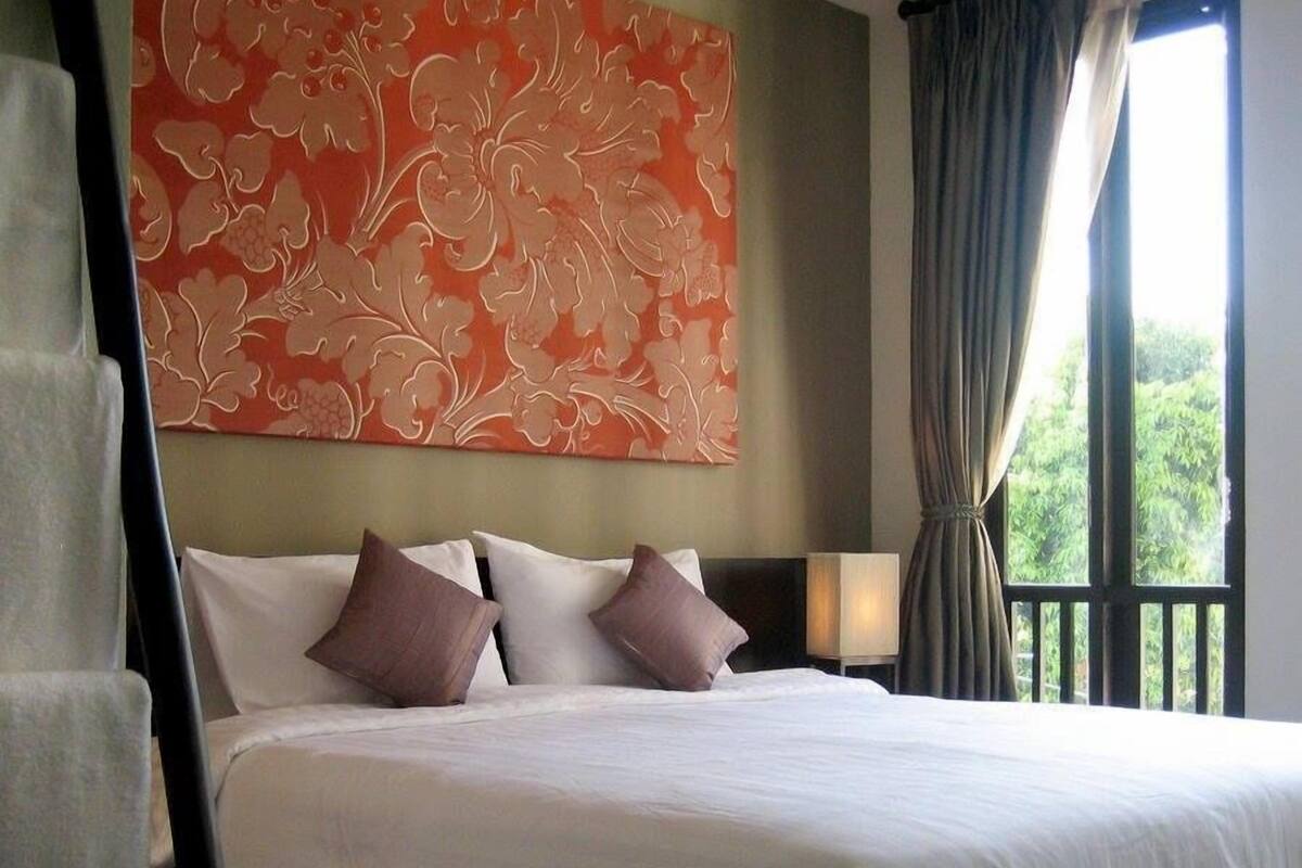 Ein Hotelzimmer mit einem großen Bett, einem Nachttisch, einer Lampe und einem Fenster mit Vorhängen.