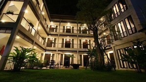 Een meerhoog hotel met balkons, buiten zitplaatsen en een goed verlichte binnenplaats.