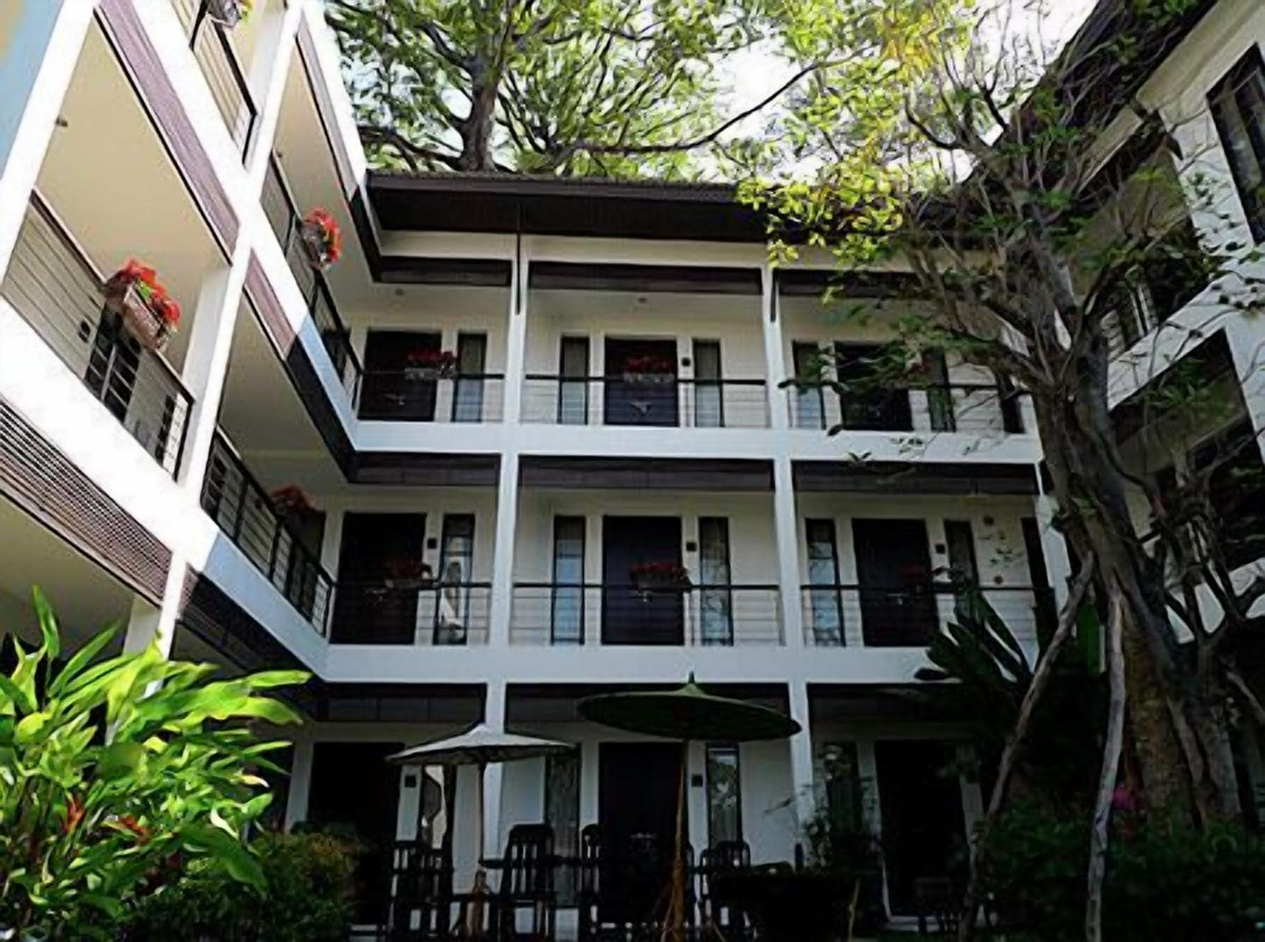 A multi-story building with balconies, outdoor seating, and a tree in the courtyard.