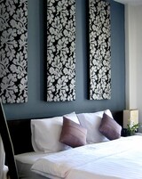 A hotel room with a bed, white bedding, and three large wall-mounted floral panels.