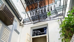 A courtyard with a small table and chairs, a potted plant, and a building entrance with a sign. - Dwell by Palanquinn (George Town)