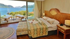 A bedroom with a large bed, a bedside table, a nightstand, a window with a view of the sea, and a small seating area with a table and chairs. - Green Nature Diamond Hotel (Marmaris)