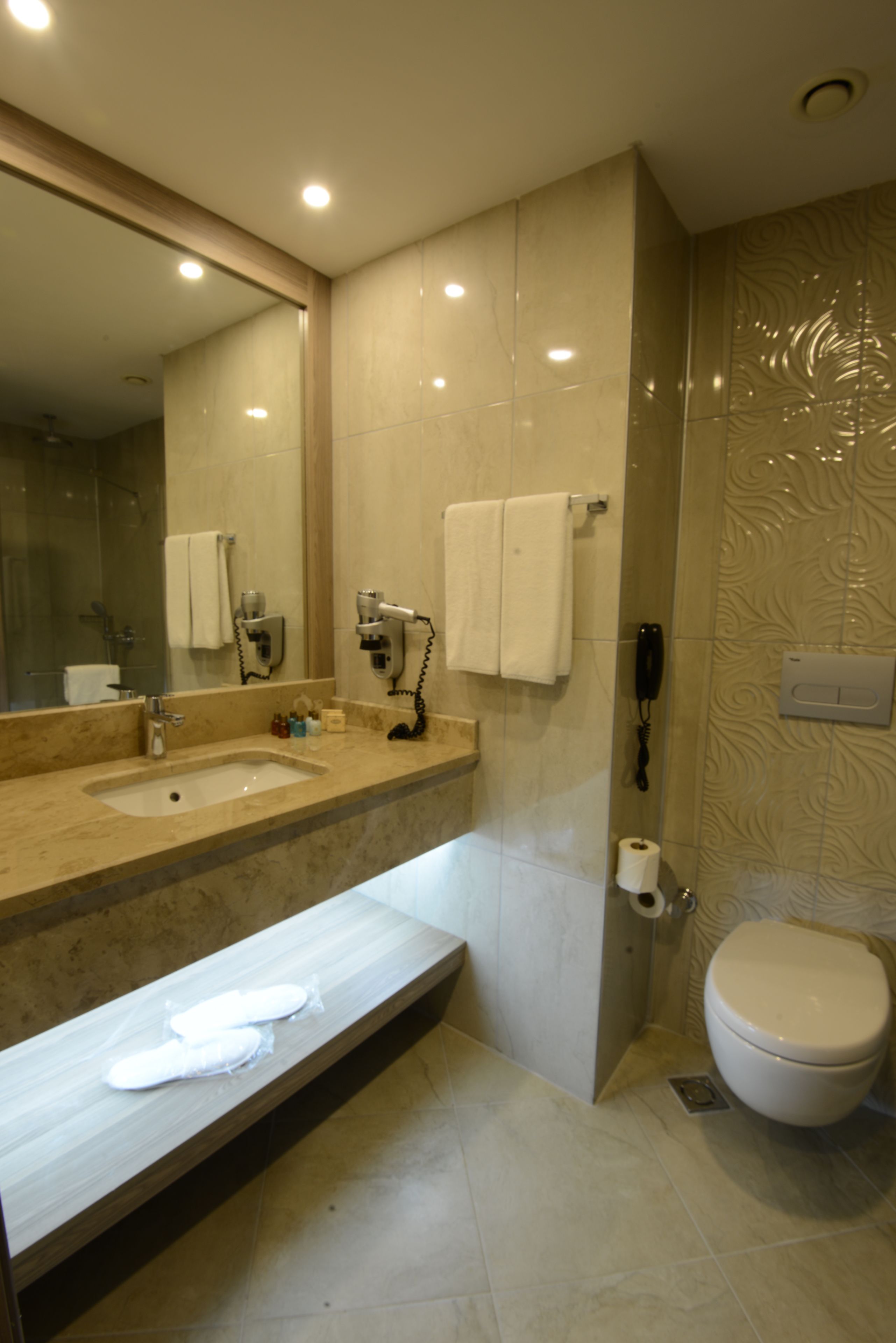 A modern bathroom with a marble sink, a large mirror, a toilet, and a shower area.
