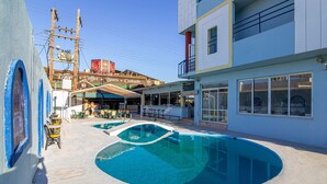 A pool area with multiple swimming pools, outdoor seating, and a building with a sign advertising coffee, beers, and cocktails. - Minoa Hotel (Hersonissos)