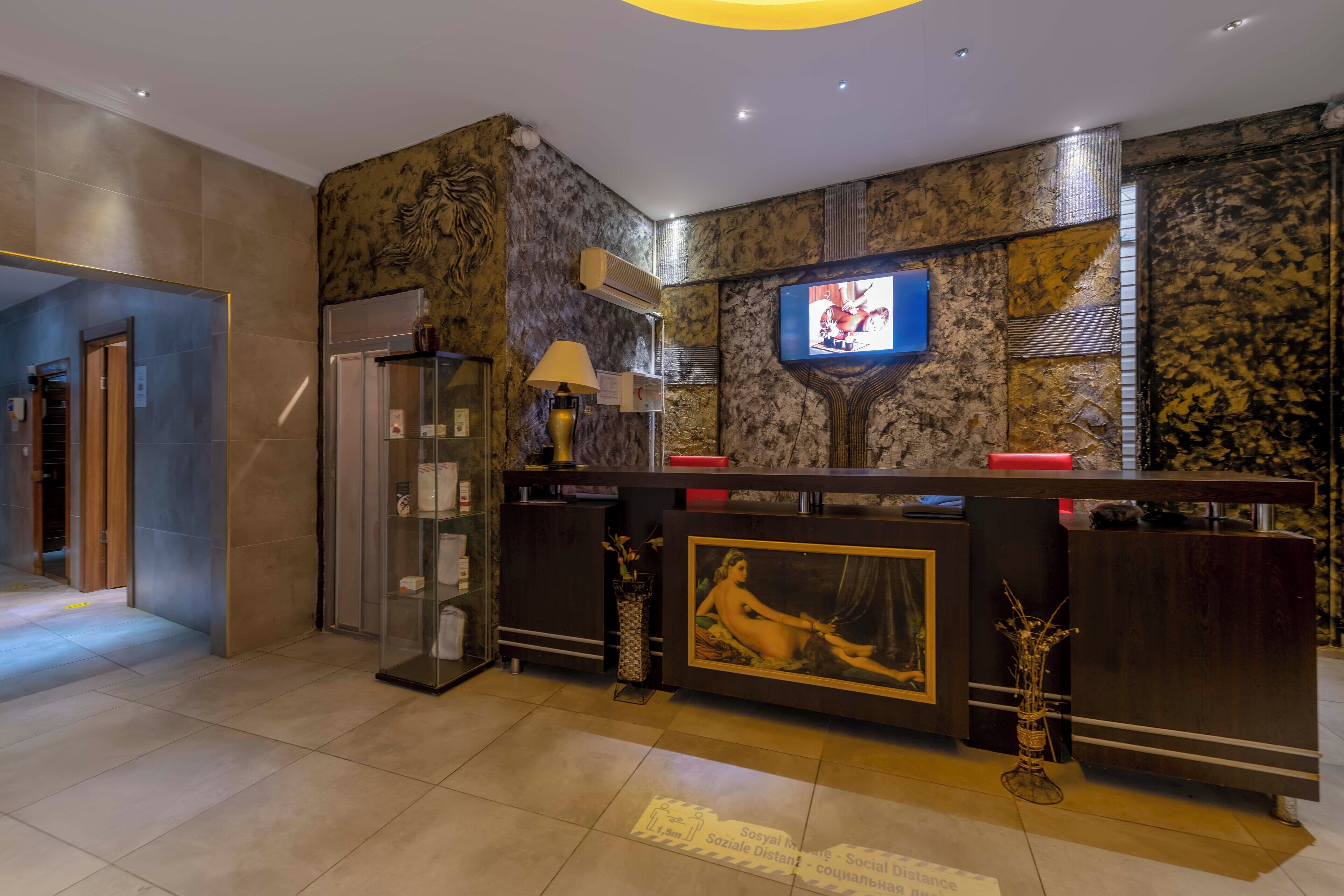 A hotel reception area with a marble wall, a television mounted above the reception desk, and a glass display case.