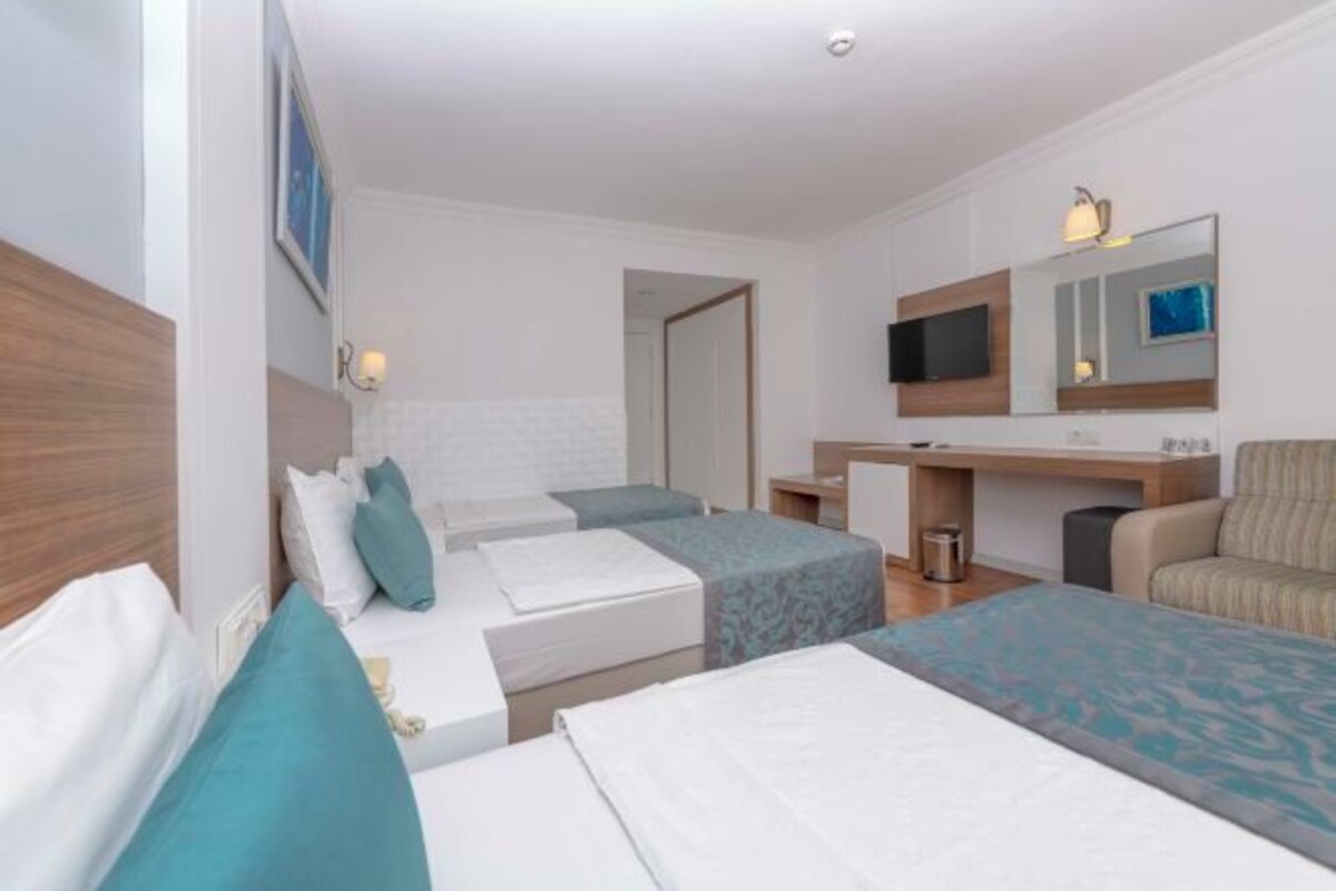 Una habitación de hotel con dos camas individuales, un sofá, un televisor y una pequeña zona de escritorio.