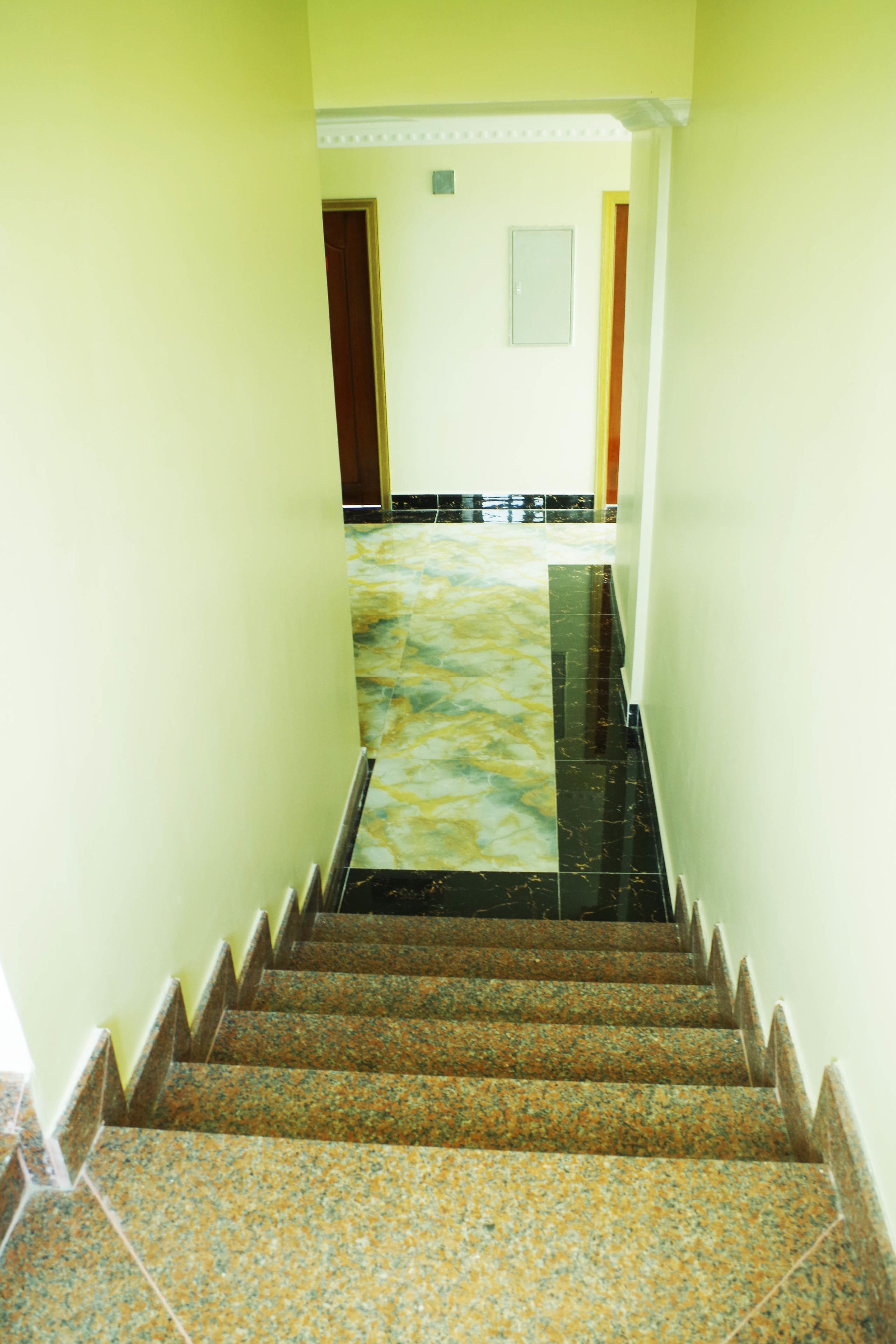 Una escalera con piso de mármol que lleva a una habitación con una puerta y un ventanal pequeño.