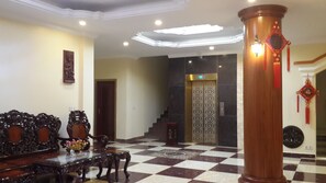 A lobby with a checkered floor, a wooden column, a staircase, and a decorative wall piece. - Golden Star Inn (Sihanoukville)