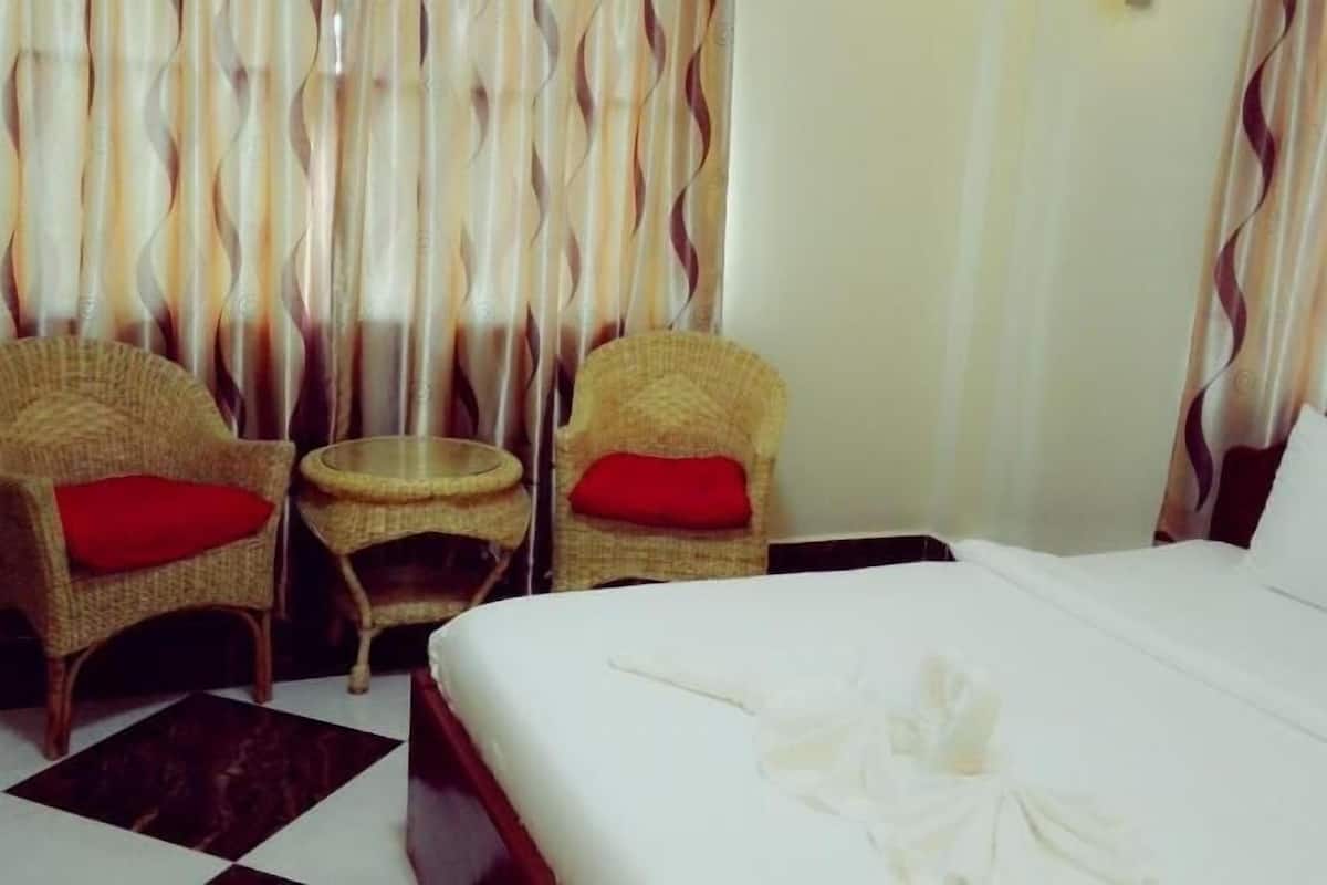 A hotel room with a bed, two wicker chairs with red cushions, a small round table, and a curtain with a wavy pattern.