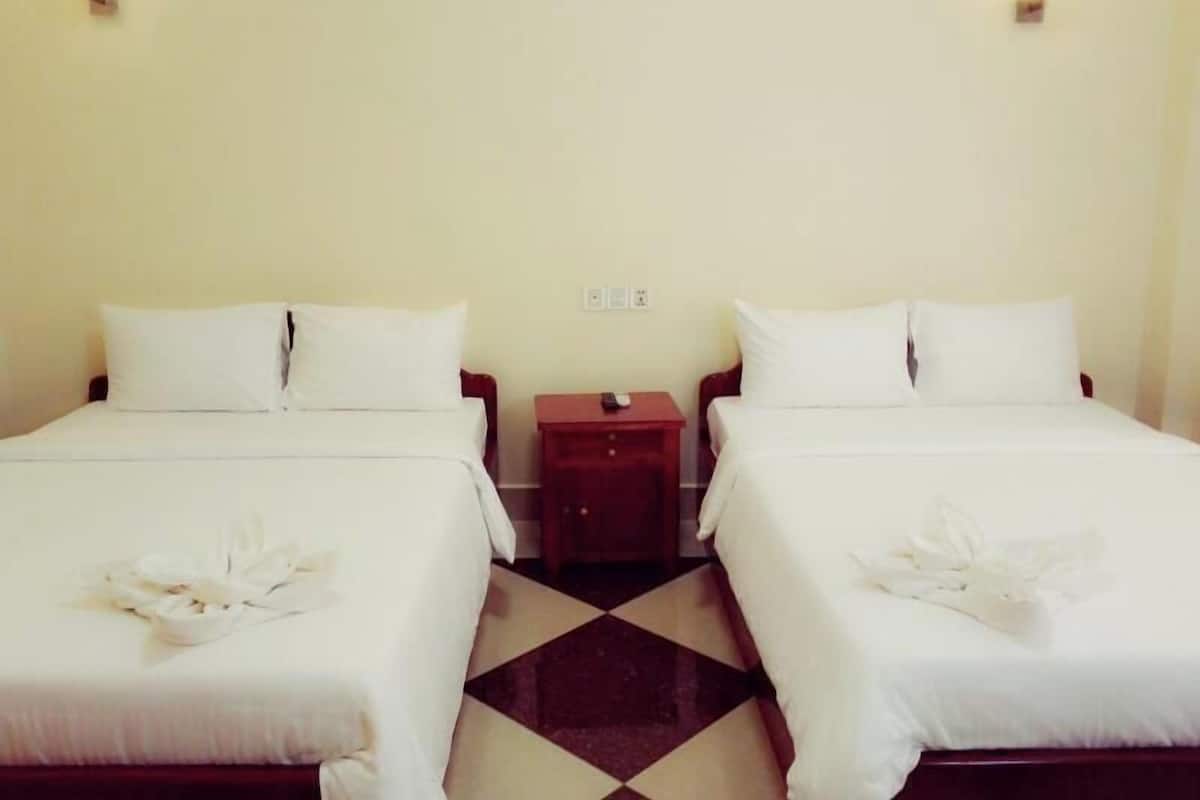 A hotel room with two beds, a small wooden nightstand, and a wall-mounted light fixture.
