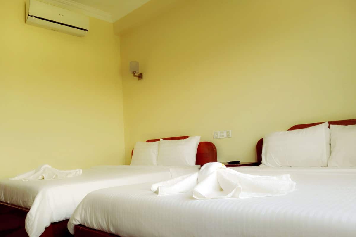 A hotel room with two beds, a wall-mounted air conditioner, and a small table with a bowl.