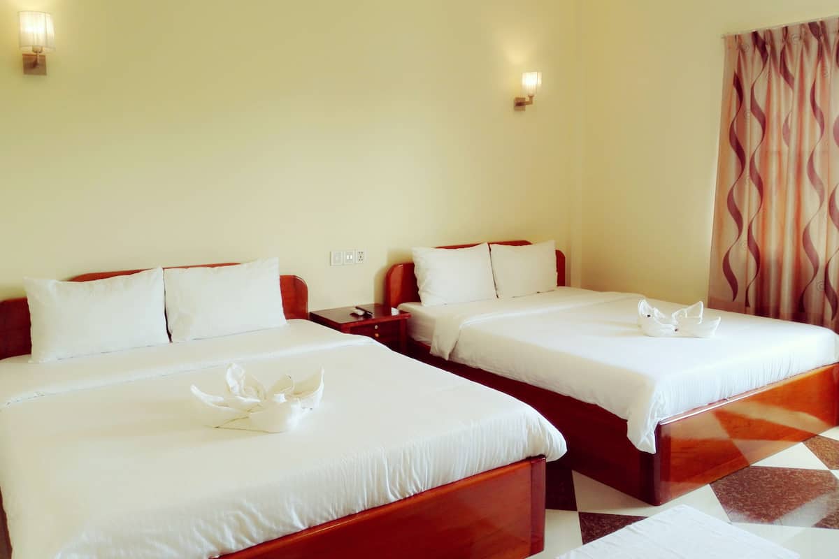 A hotel room with two beds, each with white linens and decorative pillows, a wooden headboard, a nightstand, and a wall-mounted lamp.