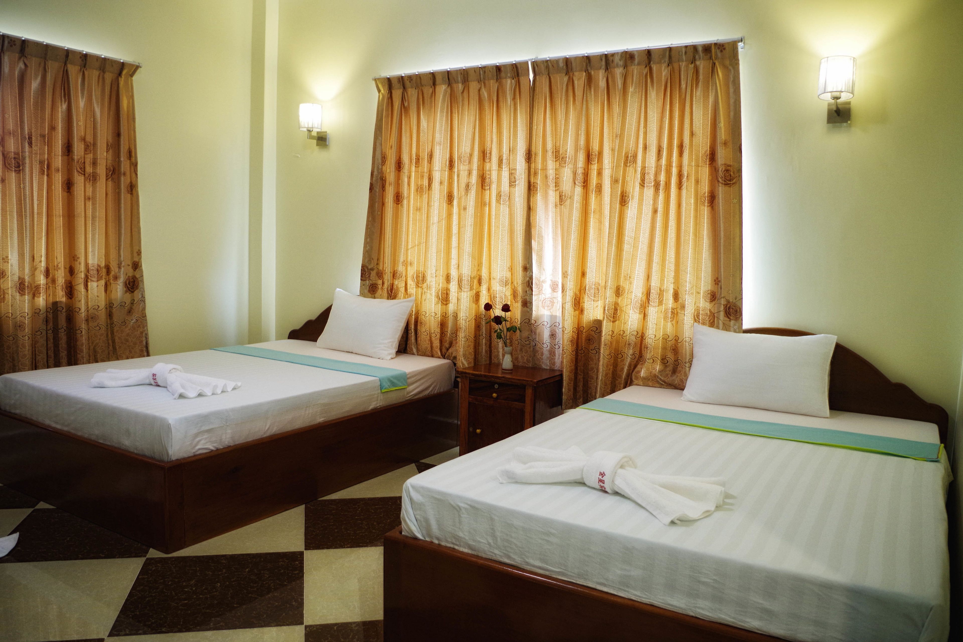 Two single beds with wooden frames, white linens, and a checkered floor pattern.