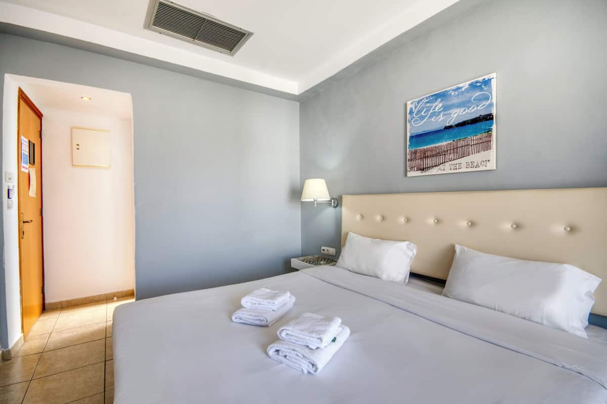 A hotel room with a large bed, a headboard, a nightstand, a lamp, and a wall with a beach-themed poster.