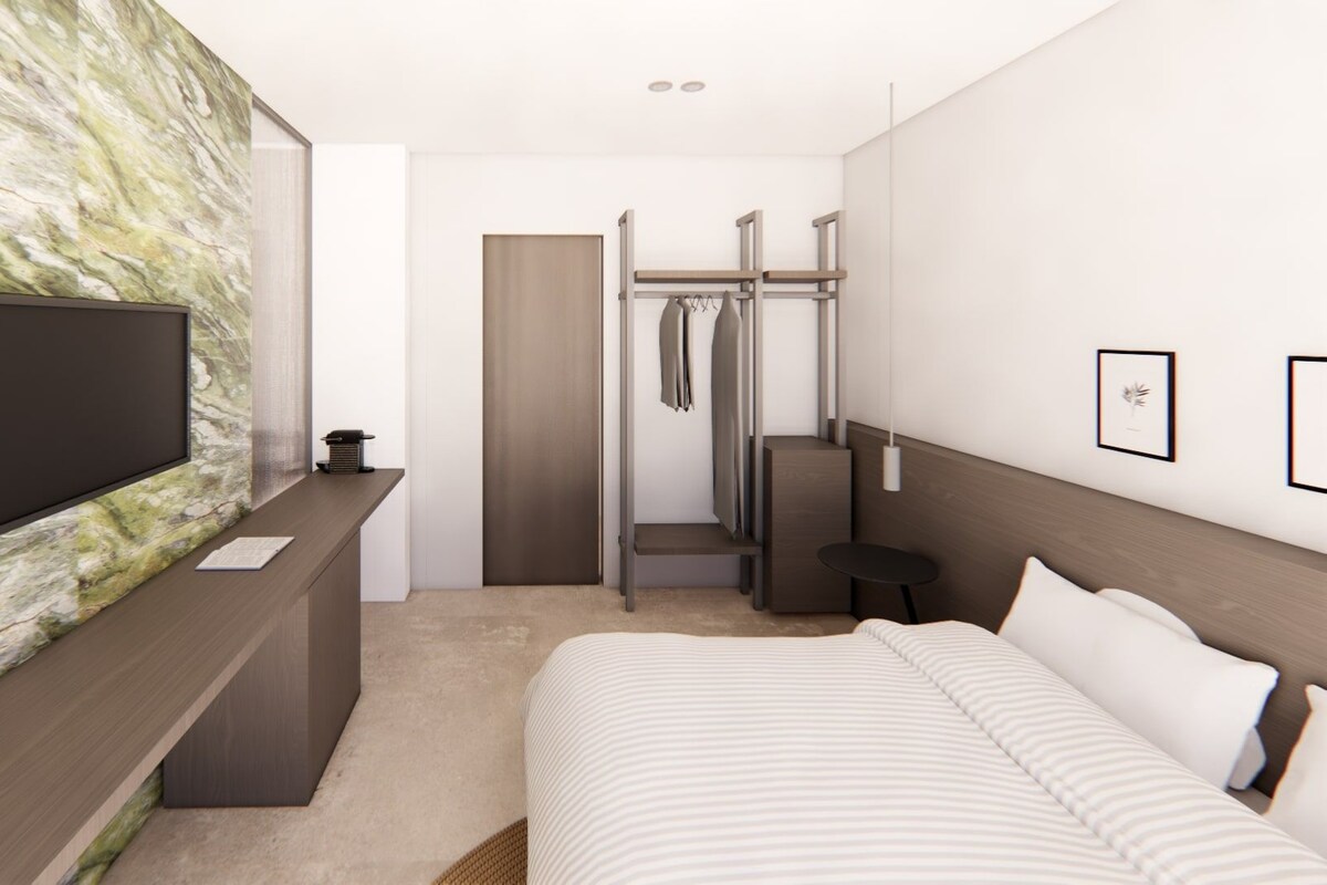 A modern hotel room with a large bed, a TV, a desk, and a wardrobe.