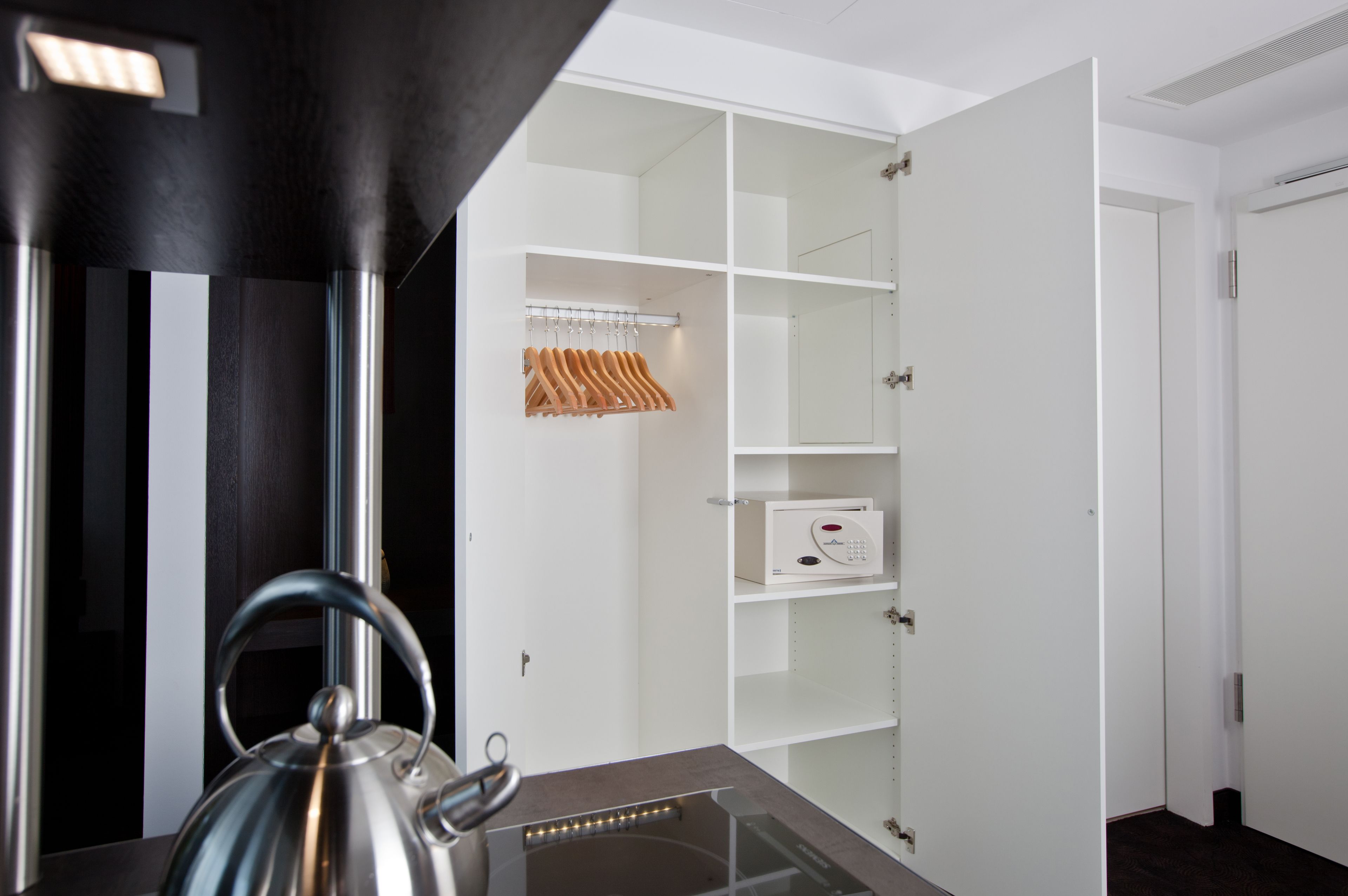 Een moderne keuken met een waterkoker op het aanrecht, een witte kast met een magnetron en een houten droogrek.