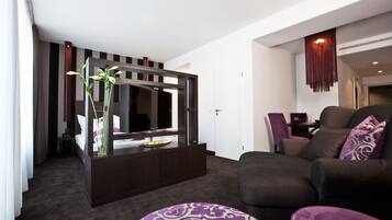 Moderni hotellihuone, jossa on tumman puun värinen konsolipöytä, suuri peili, sohva ja kuviollinen rahi.