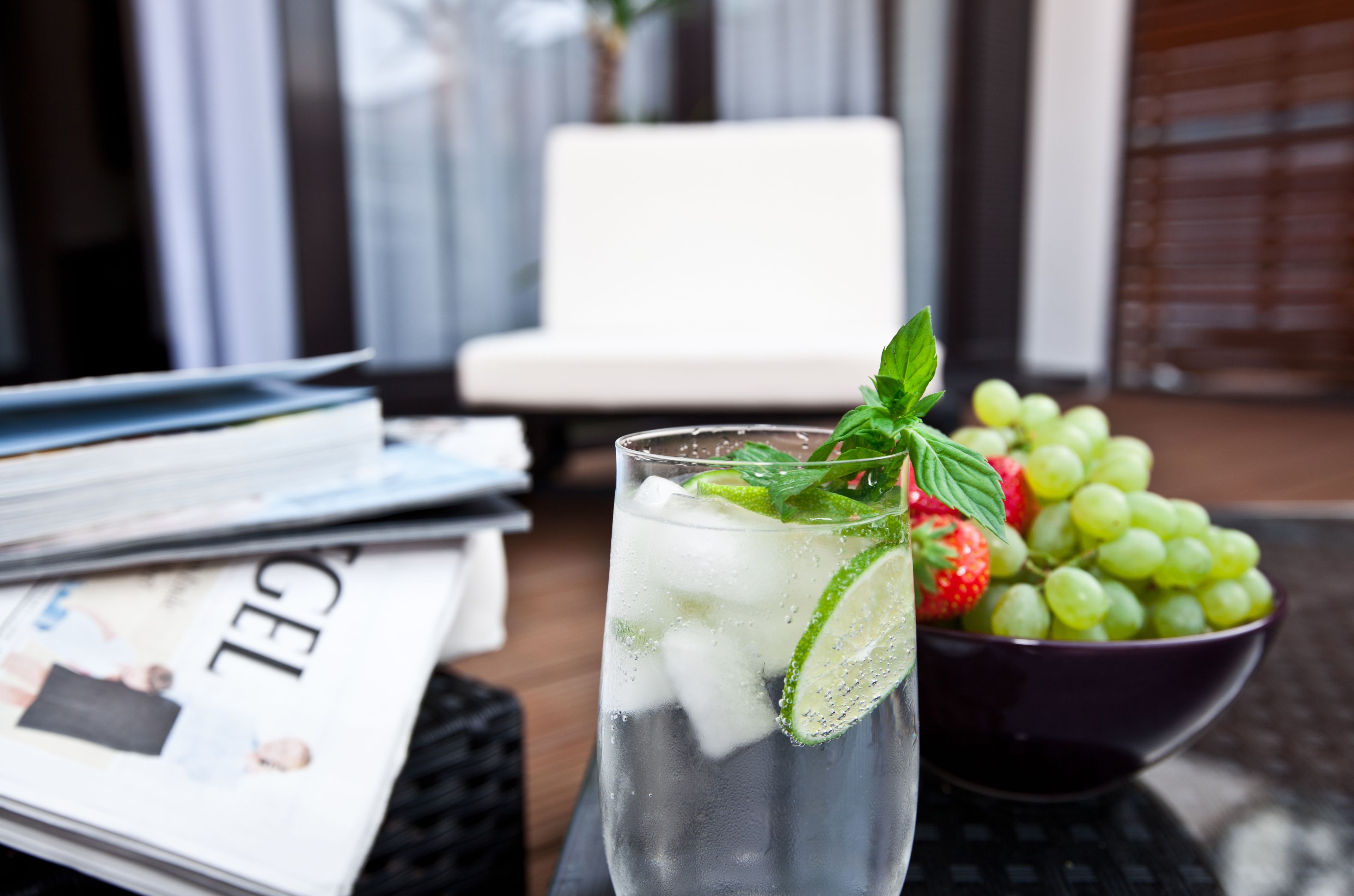 Ein Glas gekühltes Getränk mit Minze und Limette, eine Schüssel mit grünen Trauben und eine Zeitschrift auf einem Tisch.