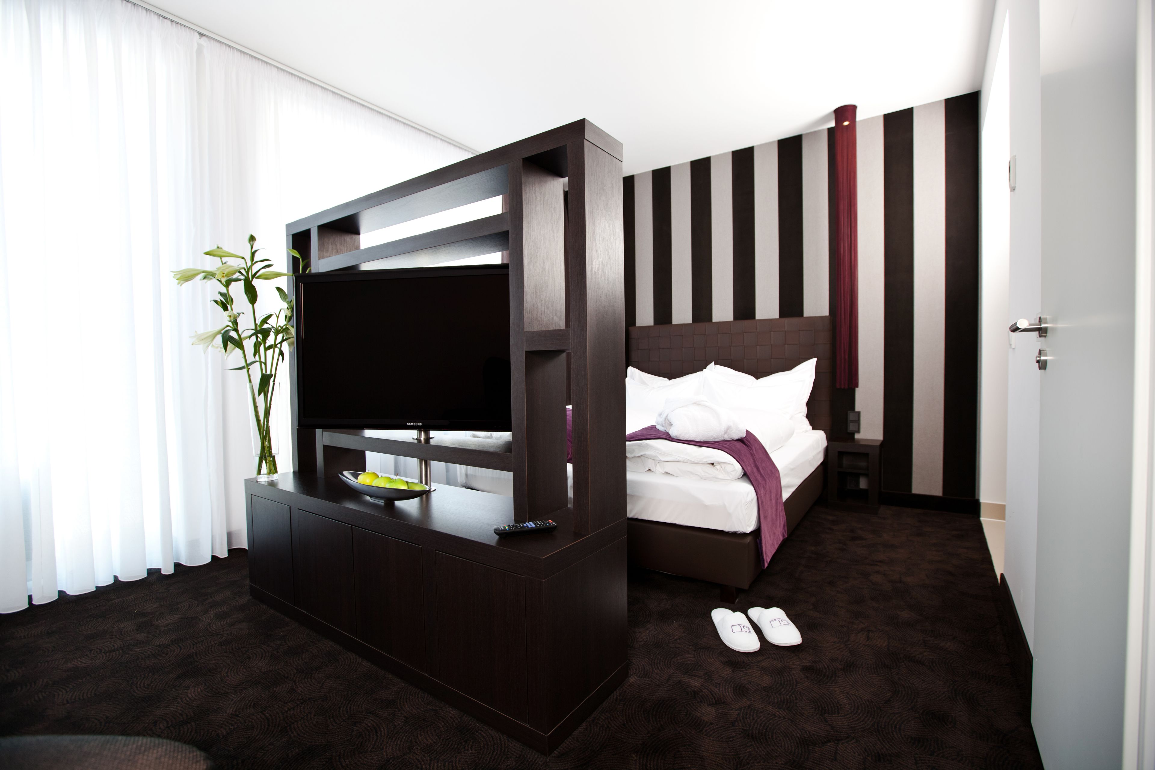 Ein Hotelzimmer mit Bett, Fernseher, Schreibtisch und Pflanze.